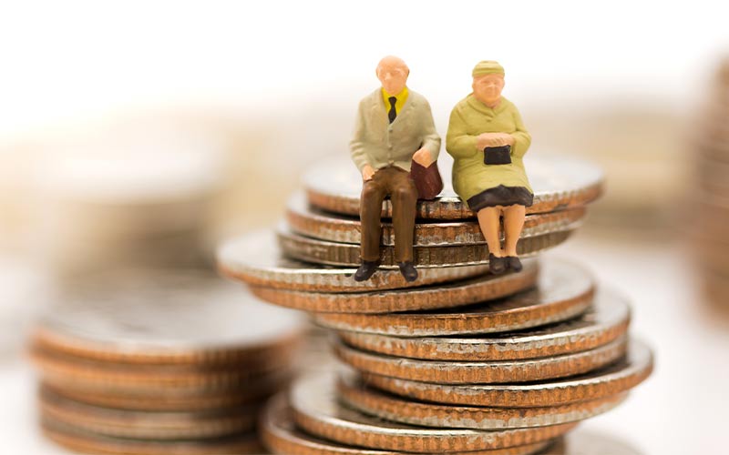 figurines of senior couple sitting on top of coins succcessful retirement